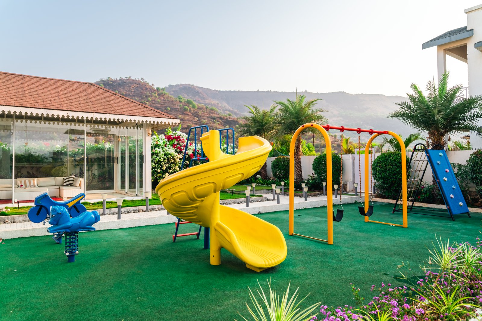KIDS' PLAY AREA – Soft astroturf, swings, slides, mid-afternoon light.